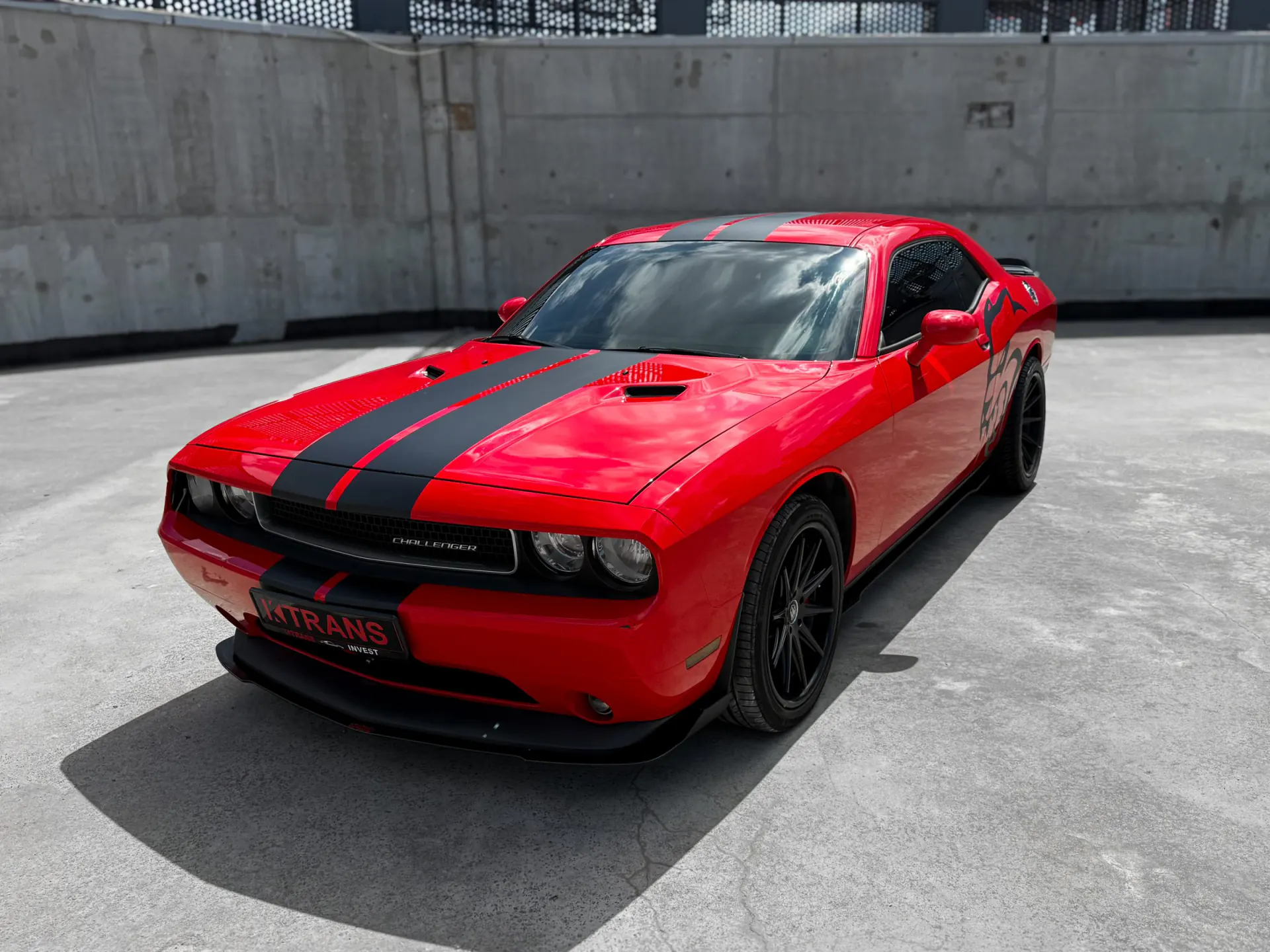 Red 2013 Dodge Challenger with black stripes and a KTRANS plate on a concrete parking garage roof